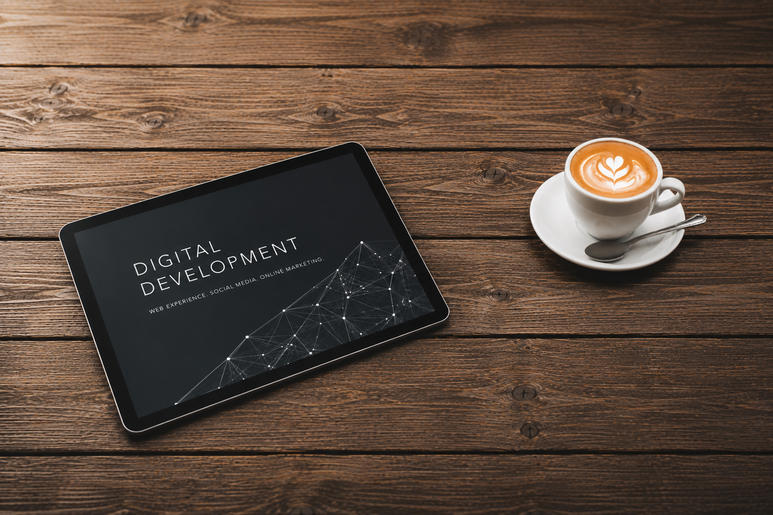 Ein Tablet mit Schriftzug Digital Development liegt neben einer Tasse Kaffee auf einem Holztisch.